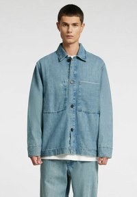 Lichtblauw denimjack met een knoopsluiting aan de voorkant, twee voorzakken en een gestructureerde afwerking. Lange mouwen en een klassieke kraag.