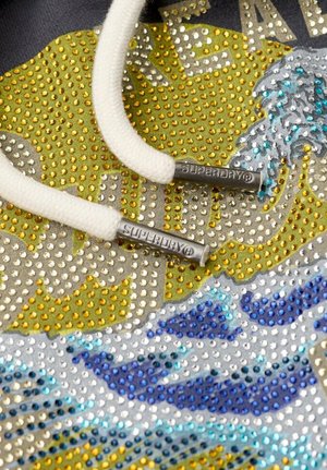 Hoodie met een gestructureerd ontwerp met zilveren, gouden en blauwe rhinestones, witte koordjes met zilveren eindstukjes en een grafisch golfpatroon.