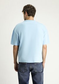 Camiseta de manga corta azul claro hecha de tela suave, con cuello redondo y corte relajado, combinada con unos pantalones vaqueros azules.