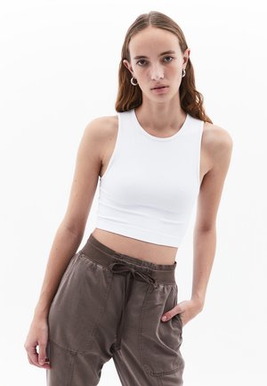 Weißes geripptes Cropped-Top mit tailliertem Design, Rundhalsausschnitt und ärmelloser Optik, kombiniert mit braunen Hosen mit Zugband und seitlichen Taschen.