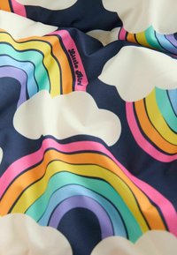 Tejido colorido con patrones de arcoíris en rosa, naranja, amarillo, verde, azul y púrpura sobre un fondo oscuro, que presenta nubes blancas.