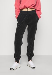 Svarta kordflöjtsbyxor med avslappnad passform, elastisk midja och dragsko. Tyget har en vertikalt ribbad textur.