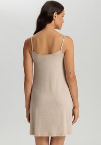 Beige cami-jurk met dunne verstelbare bandjes, een losse pasvorm en een gladde textuur, die net boven de knie valt.