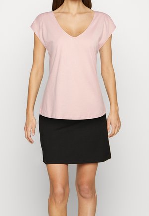 Camiseta de cuello en V color rosa claro con mangas cortas; combinada con una falda negra. Hecha de una tela suave, presenta un ajuste holgado y un diseño sencillo.