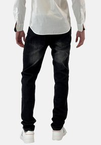 Jeans de mezclilla negra con un ajuste slim, un desvanecimiento sutil, bolsillos traseros y un ligero estiramiento, combinados con zapatillas blancas.
