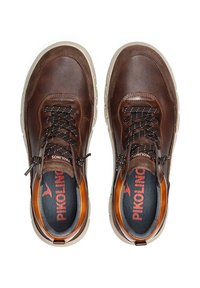 Baskets en cuir marron avec une surface texturée, une semelle en caoutchouc plus claire en contraste et des lacets noirs, avec un logo sur les semelles intérieures.