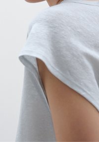 Vaaleanharmaa puuvillapaita, jossa on rento malli, näkyvät ompelusaumat ja leveä pääntie, joka paljastaa osittain olkapään.