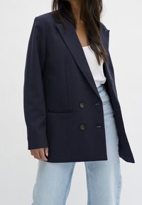 Marinblå blazer med skräddarsydd design, utrustad med notchad krage, två knappar och sidfickor, kombinerad med ljusblå denimjeans.