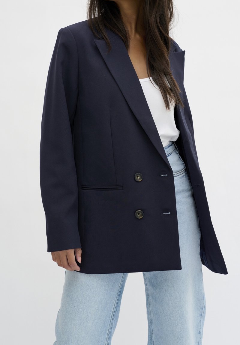 Marinblå blazer med skräddarsydd design, utrustad med notchad krage, två knappar och sidfickor, kombinerad med ljusblå denimjeans.