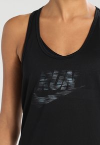 Débardeur de sport noir avec col en V, en matériau lisse, avec un graphisme texturé "RUN" et le swoosh Nike en gris foncé.