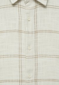 Camisa beige claro abotonada, con una tela texturizada que presenta un patrón de cuadrícula formado por líneas marrones sutiles y botones crema.