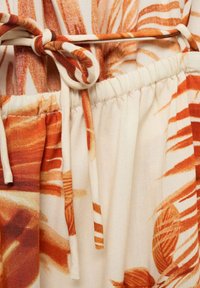 Tissu à motif floral avec des tons orange et crème, doté d'une taille élastique et d'un détail noué, présentant une surface lisse et texturée.