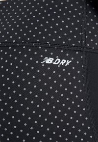 Svart idrottstyg med små silverpunkter, med platta sömmar och en "BDRY"-logotyp i vitt, vilket indikerar fukttransporterande egenskaper.