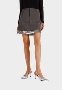 Gonna grigia con orlo di paillettes, abbinata a scarpe con tacco argentate. L'outfit presenta una forma strutturata e una texture liscia.