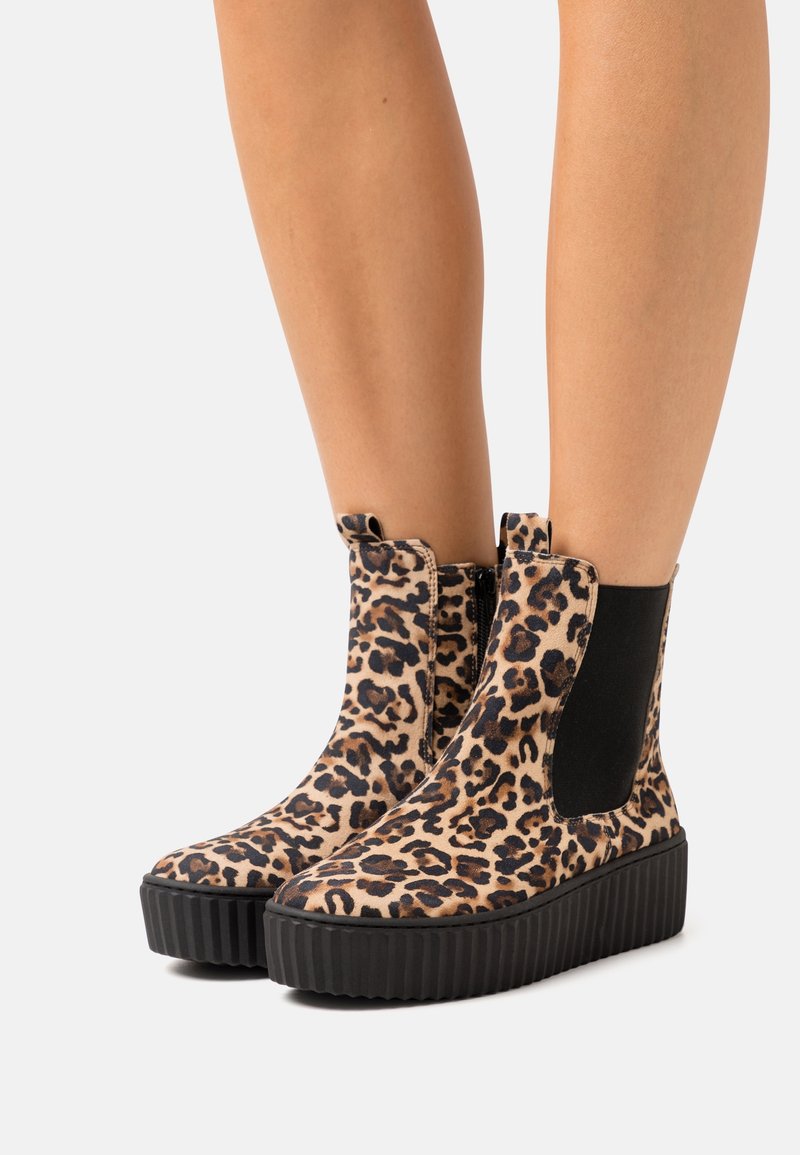 Jambes portant des bottines plateformes montant jusqu’aux chevilles avec imprimé léopard, panneaux latéraux élastiques noirs et semelles épaisses noires nervurées.