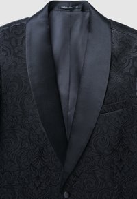 Giacca da smoking nera con motivi a spirale in rilievo. Rever a scialle in raso e una tasca sul petto. Tessuto testurizzato con accenti lisci.