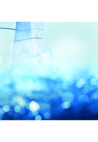 Blurred blue water with reflections and partial view of a sunlit sailboat with white sails in calm conditions.