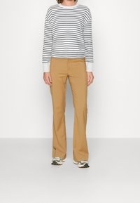 Maglione a righe bianco e blu navy a maniche lunghe abbinato a pantaloni chiari svasati. Caratterizzato da polsini a coste e una vestibilità rilassata. Scarpe sportive argento visibili.