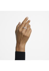 Silberner Ring mit mehreren kleinen klaren Edelsteinen, in einem zarten, geschwungenen Design gefasst. Die Hand ist vor einem schlichten weißen Hintergrund abgebildet.