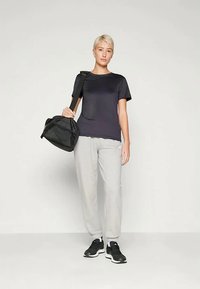 Svart t-skjorte med korte ermer, grå joggebukser og svarte sneakers; bærer en svart treningsbag. Enkelt design, lett materiale, nøytrale farger.