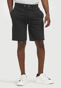 Mustat puuvillashortsit, joissa on joustava vy�ötärö, nyöri ja sivutaskut, yhdistettynä valkoisiin lenkkikenkiin ja harmaaseen paitaan.