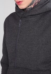 Ciemnoszara bluza z zamkiem błyskawicznym o miękkiej fakturze, z wysokim kołnierzem i kieszenią kangurką, z wyraźnym przeszyciem i gładkim zamkiem.