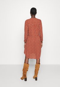 Vestido rojo con estampado, mangas largas, cinturón en la cintura y largo hasta la rodilla; combinado con botas marrones de ante hasta la rodilla con tacón ancho.