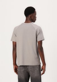 Grå kortærmet t-shirt med rund hals, der har raglanærmer og en glat tekstur, parret med mørke jeans.