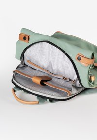 Grüne Stofftasche mit sandfarbenen Lederakzenten. Das Innere verfügt über ein gittermusterförmiges Futter, ein Hauptfach und eine zusätzliche Tasche.