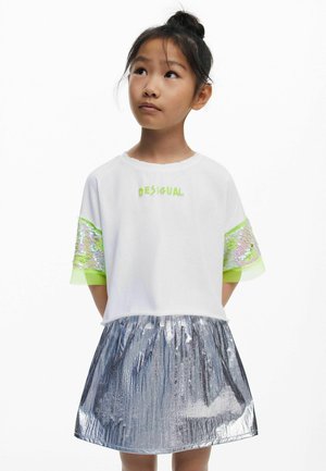 Witte T-shirt met groene letters, doorschijnende mouwen versierd met pailletten, gecombineerd met een metallic zilveren rok met een gekreukte textuur.