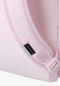 Rosa Stoff-Rucksack mit strukturierter Oberfläche, ausgestattet mit einem schwarzen Markenlabel und einem verstellbaren Riemenverschluss.