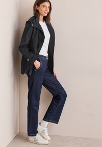 Svart lättviktsjacka med huva, vit t-shirt, mörkblå raka jeans och vita sneakers med gröna detaljer.