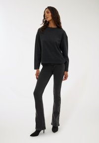 Ciemnoszary sweter przez głowę z okrągłym dekoltem i opuszczonymi ramionami, w połączeniu z czarnymi dzwonami i czarnymi, spiczastymi szpilkami. Gładka tekstura.