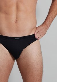 Schwarze Herrenunterwäsche aus glattem Stoff, mit einem taillierten Design, einem elastischen Bund und einem Logoplatz auf der Vorderseite.