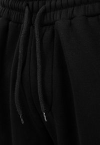 Nærbillede af linningen på sorte joggingbukser med elastik og sorte snore med metalspidser.