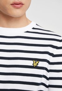 Maglione a righe con collo rotondo in bianco e blu navy, caratterizzato da un tessuto testurizzato e un piccolo logo ricamato giallo sul petto.