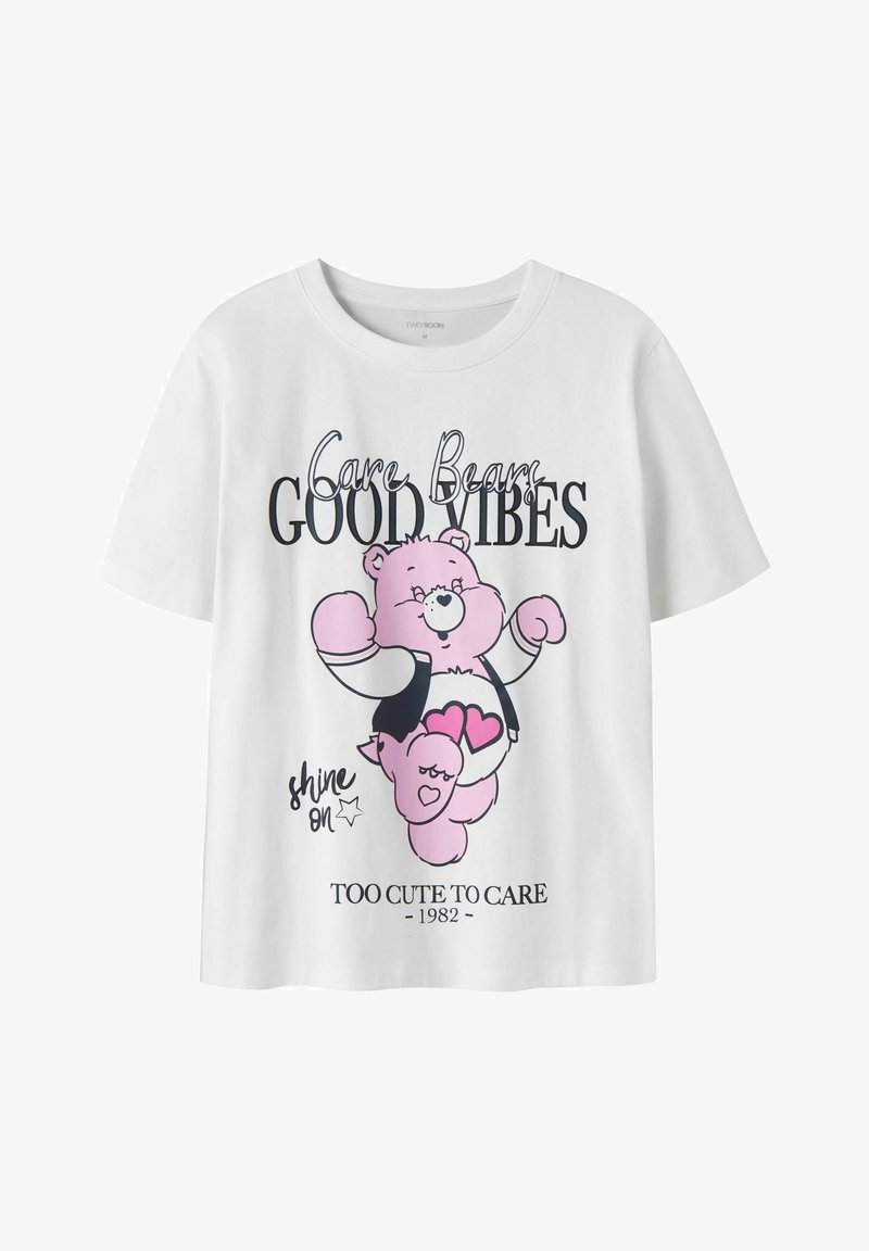 Λευκό T-shirt με ροζ γραφικό Care Bear και κείμενο "Care Bears Good Vibes," "shine on," και "Too Cute to Care 1982" μπροστά.