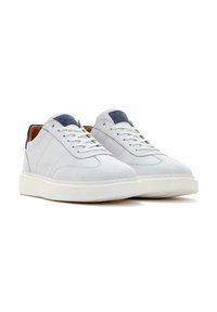 Baskets blanches en cuir avec des accents bleu marine, des lacets et une semelle en caoutchouc texturée. Présente une surface lisse et un design épuré.