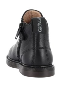Stivale nero in pelle alla caviglia con cerniera laterale, linguetta etichettata "GRÜNLAND" e suola cucita vista da dietro.
