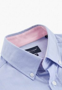 Chemise bleue claire à boutons avec un col intérieur rose, faite en coton, présentant une texture lisse et un motif subtil, avec deux boutons blancs.