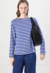 Long-sleeve striped shirt in blue and white with a boat neckline, paired with blue pants and a black sling bag. Smooth cotton fabric.