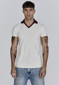 Crème polo shirt met een bordeauxkleurige kraag en een V-halsontwerp. Heeft een getailleerde pasvorm en een subtiele logodetail op de borst.