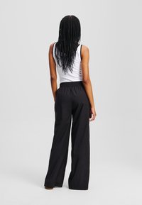 Zwarte wijde broek met een elastische tailleband, gecombineerd met een aansluitend wit tanktop. De stof ziet er licht en soepel uit.