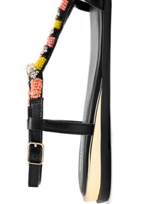 Sandal plana negra con una tira de cuentas colorida que presenta acentos en rosa, amarillo y blanco, detalle en tono dorado en la suela, hebilla ajustable en el tobillo.