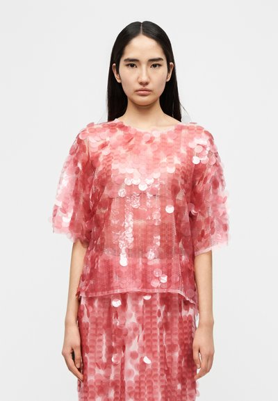 Ροζ διάφανο τοπ με κυκλικές παγιέτες, άνετη εφαρμογή, κοντά μανίκια και στρογγυλή λαιμόκοψη, σε συνδυασμό με φούστα με παγιέτες στο ίδιο σχέδιο.