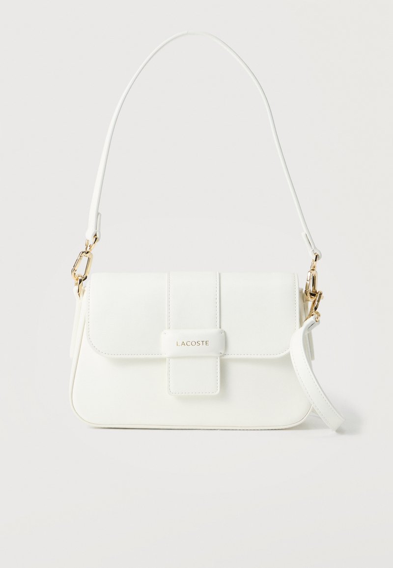 Λευκή δερμάτινη τσάντα ώμου Lacoste με κλείσιμο με καπάκι, εξαρτήματα σε χρυσό χρώμα και αποσπώμενο λουράκι σε μονόχρωμο φόντο.