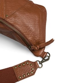 Sac en cuir marron avec une surface texturée, fermeture zippée et une bandoulière dotée de rivets. Le design est triangulaire avec une fermeture éclair sombre.