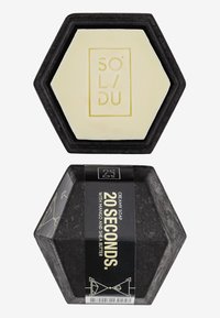 Hexagonal soap in cream with a black base. Label in black with gold text stating "20 SECONDS." Features decorative geometric accents.