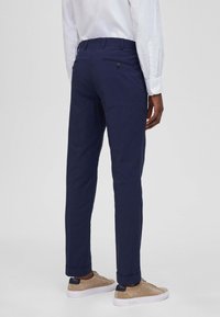 Chino blu navy con finitura testurizzata, dotati di una vita liscia, orli risvoltati e una tasca posteriore con dettaglio a bottone.