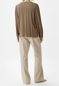 Blouse marron à manches longues avec des épaules plissées, associée à un pantalon beige à jambes larges, présentant un motif texturé et une finition en tissu lisse.